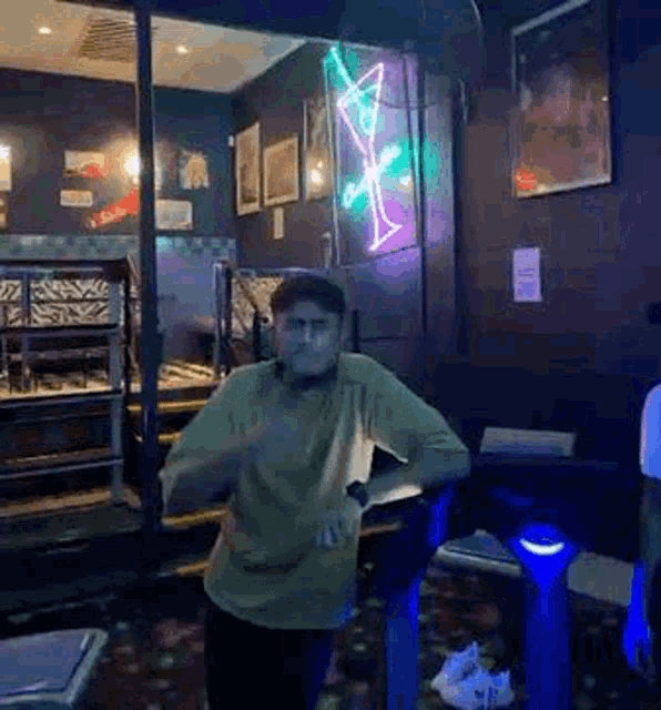 a man is dancing in a dark room with a neon sign on the wall .
