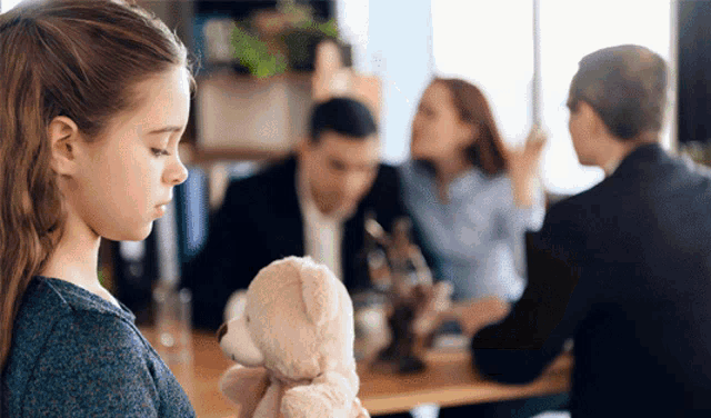 a little girl is holding a teddy bear in front of a group of people