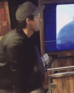 a man wearing a hat is looking at a tv screen