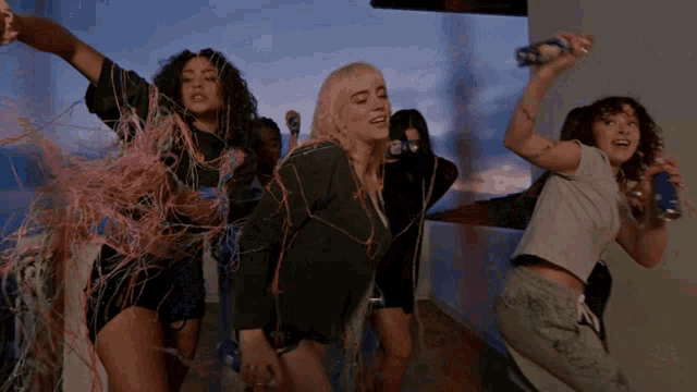 a group of women are dancing and one is holding a can of red bull .