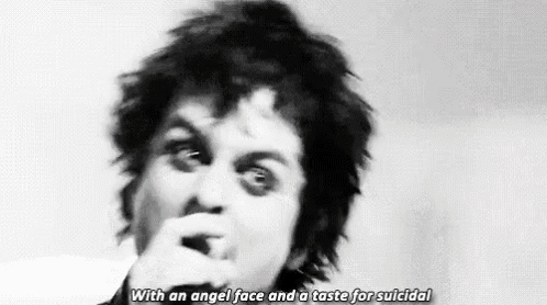 a man with an angel face and a taste for suicide is singing into a microphone in a black and white photo .
