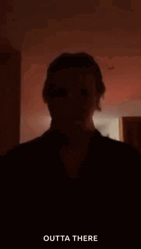 a silhouette of a person standing in a dark room with the words `` outta there '' written on the bottom .