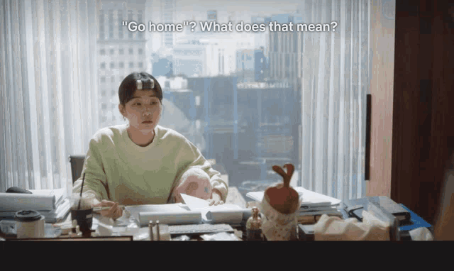 a woman sits at a desk with the words go home what does that mean written above her