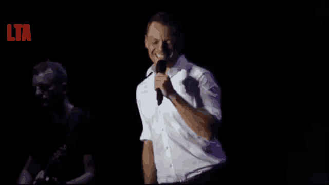 a man in a white shirt is singing into a microphone on a stage with the letters lta on the bottom