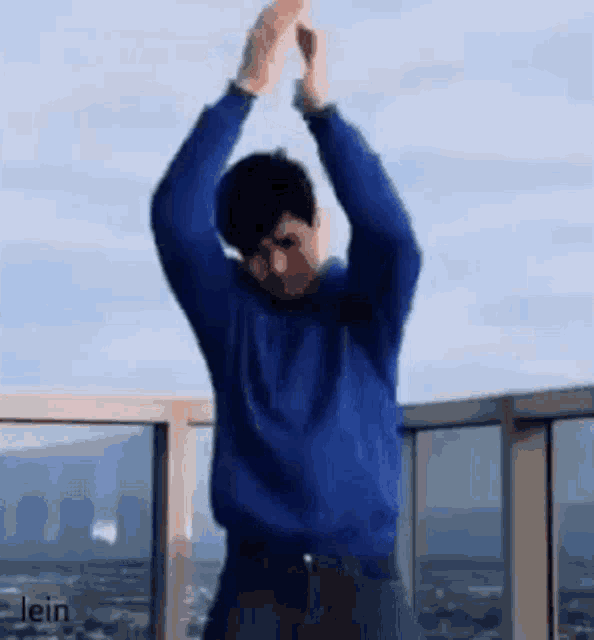 a man in a blue sweater is dancing on a balcony with his hands in the air .