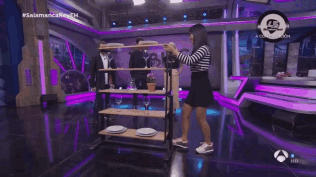a woman in a black and white striped skirt is dancing in front of a table with plates and wine glasses on it