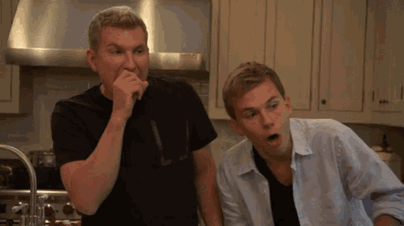 two men are standing in a kitchen with one covering his mouth
