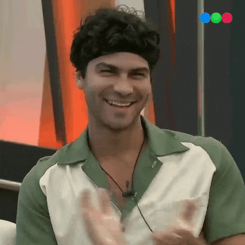 a man in a green and white shirt is smiling and clapping his hands