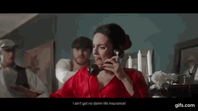 a woman in a red dress is talking on a telephone while a man looks on .