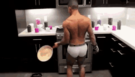 a shirtless man in underwear is holding a frying pan in a kitchen .