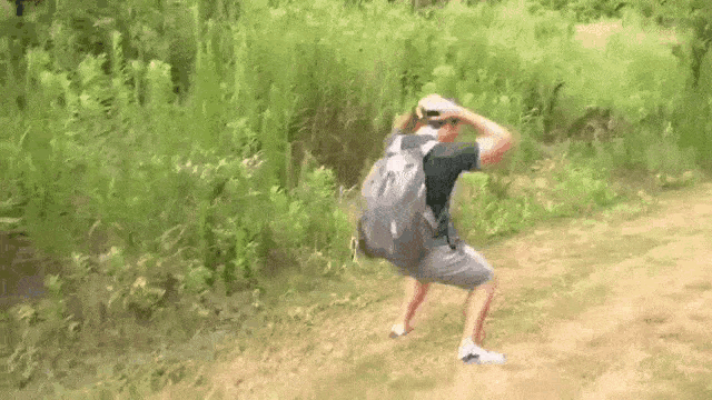 a man with a backpack is squatting on a dirt path .