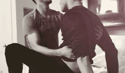 a man is sitting on another man 's lap while they kiss .