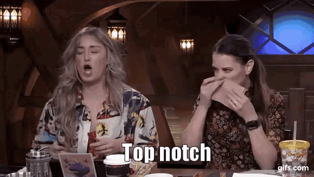 two women are sitting at a table with their mouths open and one of them is holding a napkin over her nose .