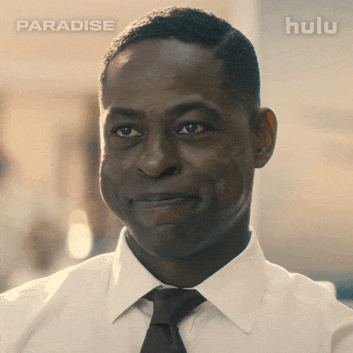 a man in a white shirt and tie is smiling in front of a hulu ad