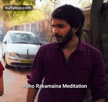 a man with a beard is standing in front of a car and talking to another man .