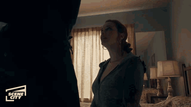 a woman is standing in a bedroom with a scene city logo in the corner
