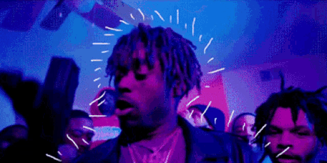a man with dreadlocks is talking on a cell phone in front of a crowd of people .