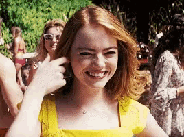 a woman in a yellow dress is smiling while standing in front of a crowd of people .