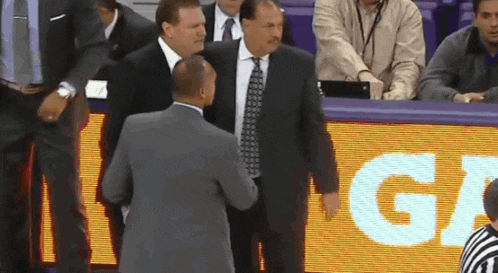 a man in a suit and tie talks to another man in front of a sign that says " ga "