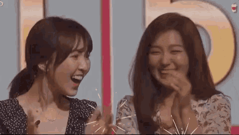 two women are standing next to each other on a stage laughing and clapping .