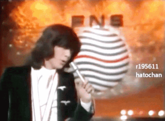 a person holding a microphone in front of a sign that says fns