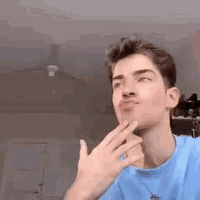 a young man in a blue shirt is making a funny face while holding his hand to his chin .