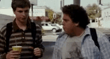 two men are standing next to each other on a street holding cups of coffee .