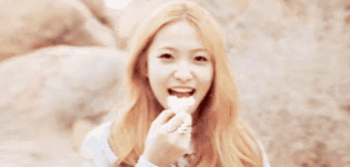 a woman with blonde hair is eating a piece of food while sitting on the ground .
