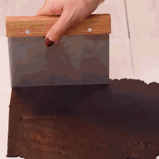 a person is using a spatula to spread a piece of brown dough