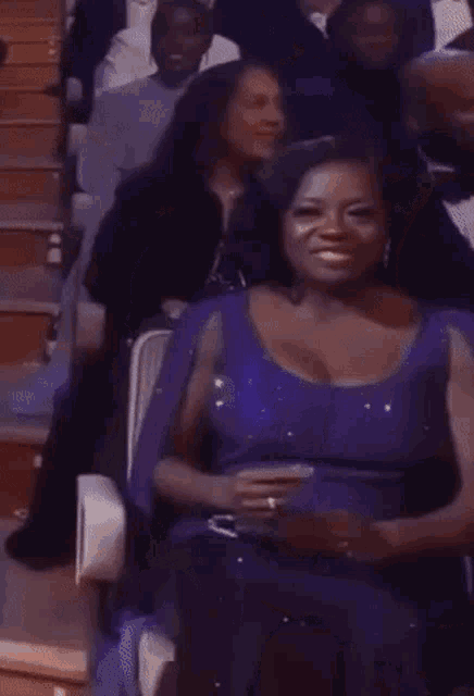 a woman in a purple dress is sitting in a stadium with other people .