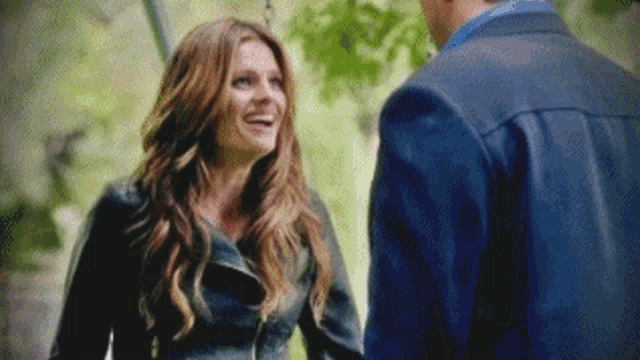 a man and a woman are standing next to each other and smiling . the woman is wearing a black leather jacket .