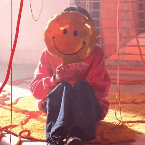 a person holding a smiley face balloon while wearing a pink sweatshirt