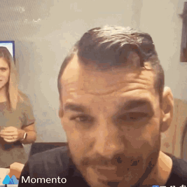 a man with a beard is looking at the camera with a woman behind him and the words momento on the bottom right