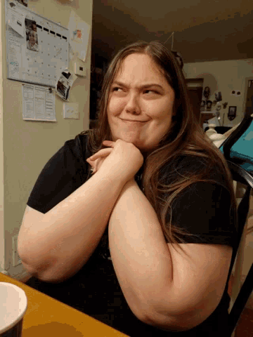 a woman is sitting at a table with a calendar on the wall