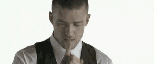 a man in a suit and tie is making a shhh gesture with his finger .