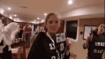 a woman holding a microphone in a room with a man wearing a shirt that says spray bau .
