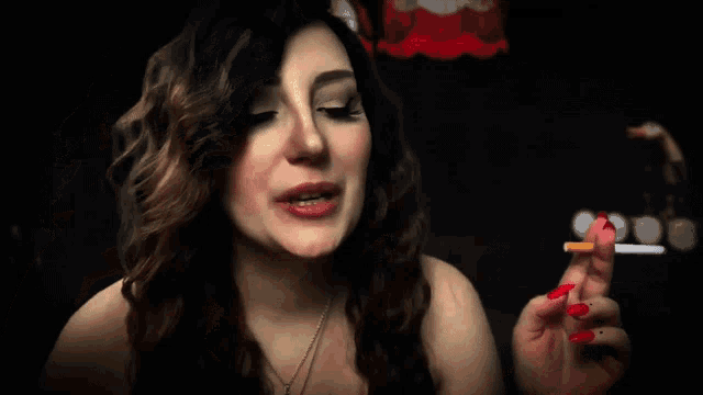 a woman with red nails is smoking a cigarette in a dark room