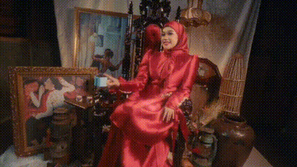 a woman in a red dress and hijab is sitting on a throne .