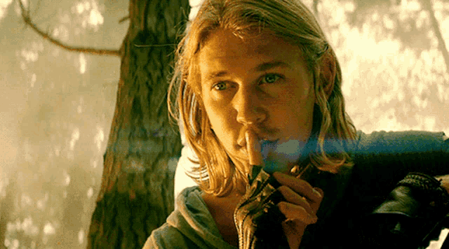 a man with long blonde hair is smoking a cigarette in the woods