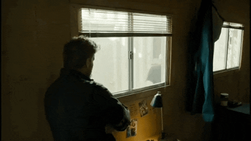 a man looking out of a window with blinds on it