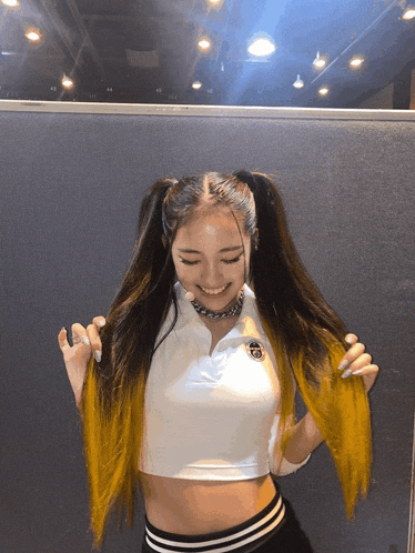 a woman wearing a white crop top and black striped pants has yellow highlights in her hair