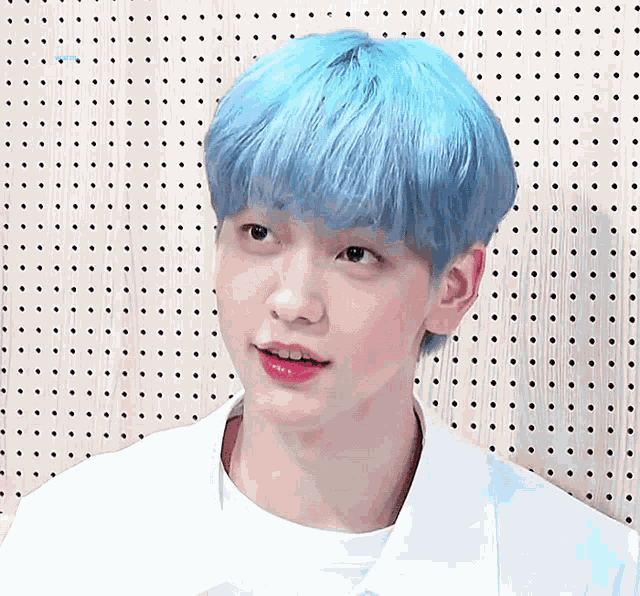 a young man with blue hair is standing in front of a perforated wall