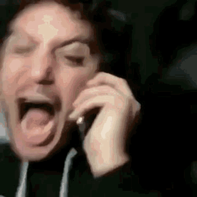 a man is talking on a cell phone with his mouth open and his eyes closed .