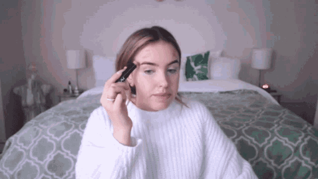 a woman in a white sweater is applying makeup