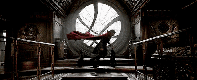 a man in a red cape is standing in front of a large window in a room .