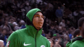 a basketball player wearing a green hoodie is standing in front of a crowd of people .