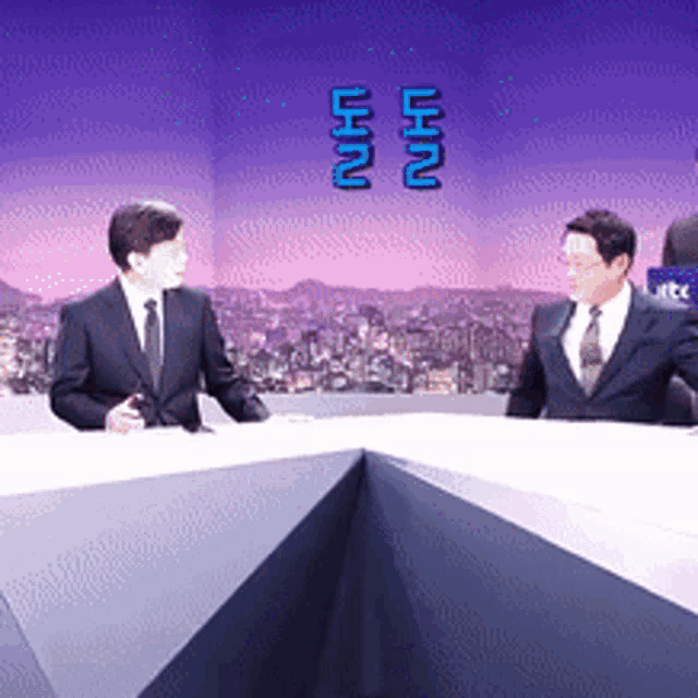 two men in suits and ties are sitting at a table with a city in the background and a sign that says uhn on it