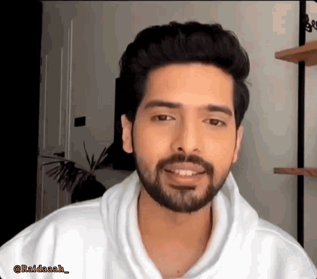 a man with a beard wearing a white hoodie is smiling .