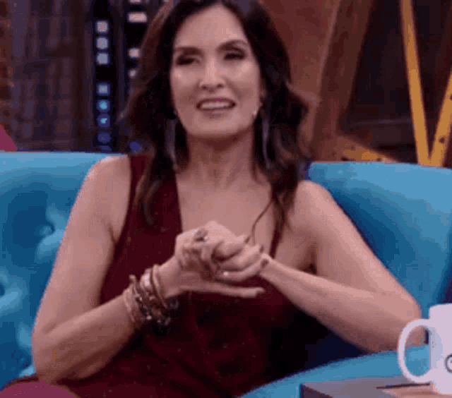 a woman in a red dress is sitting on a blue couch with her hands folded .