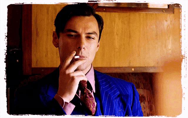 a man wearing a blue suit and tie smoking a cigarette
